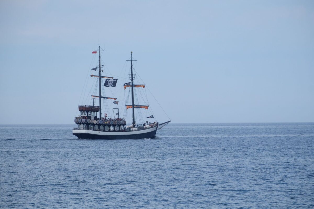 A vintage pirate ship with sails unfolds on calm ocean waters under a clear sky.
